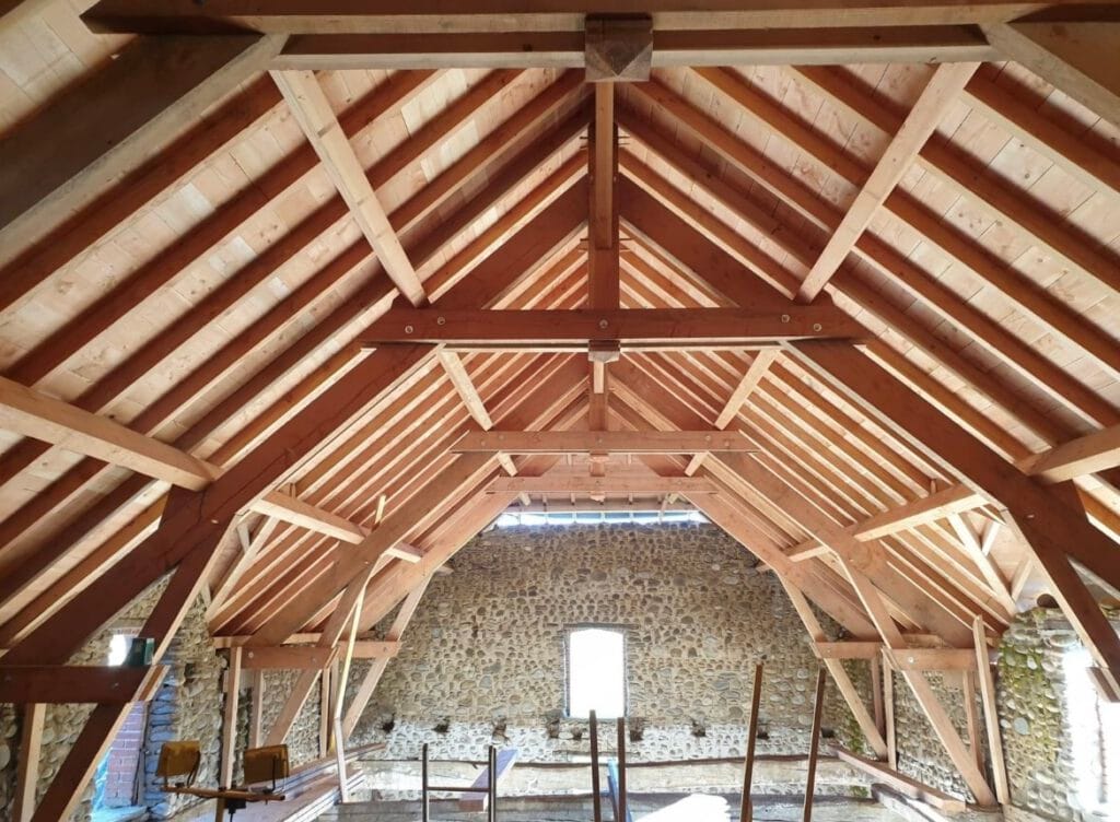 Fermes de toit en bois et murs en pierre dun grenier inachevé, avec lumière entrant par les fenêtres.