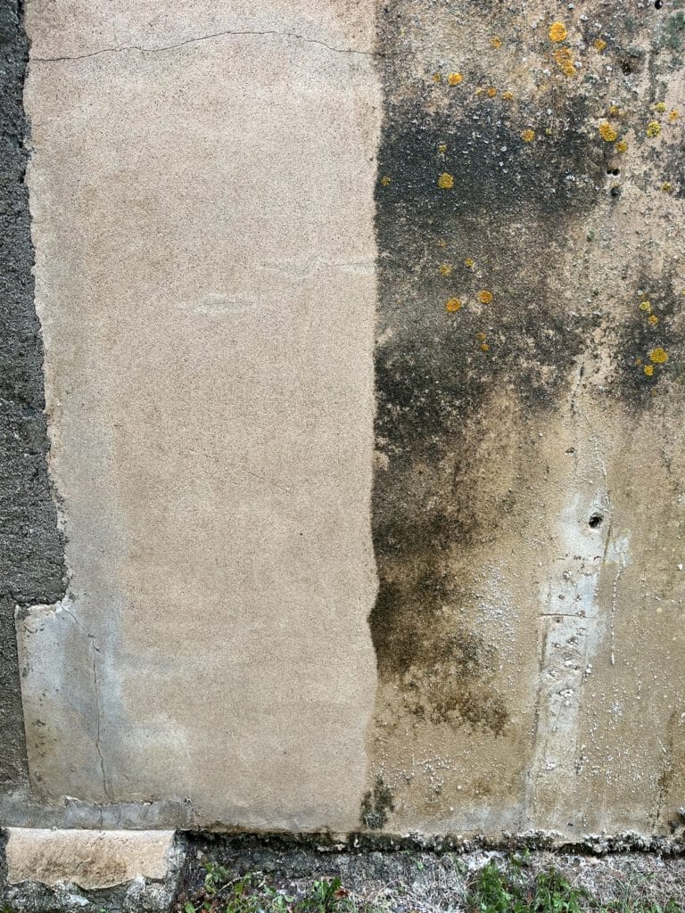 Image dun mur de béton mettant en valeur Nos réalisations : une surface propre à gauche contrastant avec une zone patinée et moisie parsemée de taches sombres et de points jaunes à droite.