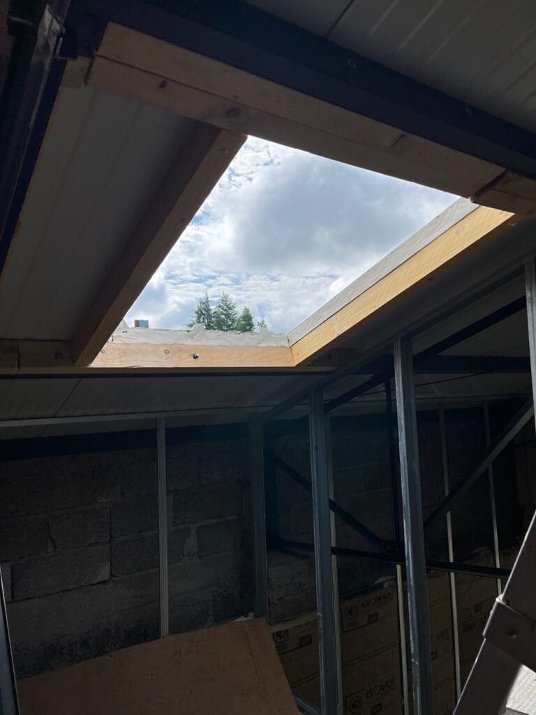 Vue partielle dun chantier avec un toit inachevé et une grande ouverture rectangulaire, dévoilant le ciel et les nuages - un aperçu dune de nos réalisations.