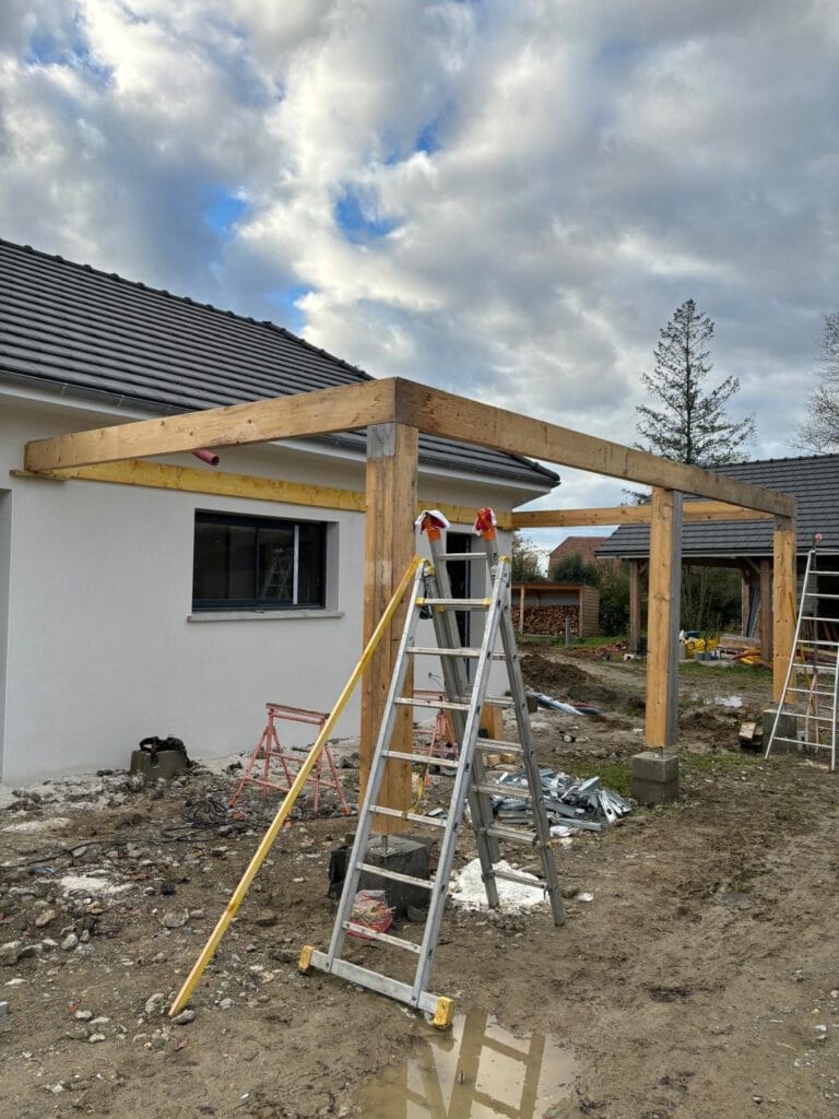 Nos réalisations : Une structure de pergola en bois est en construction dans une cour arrière, entourée déchelles et doutils. Le ciel nuageux au-dessus ajoute une touche dramatique à cet ambitieux projet de rénovation domiciliaire.